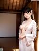 A woman in a white kimono standing in front of a window.